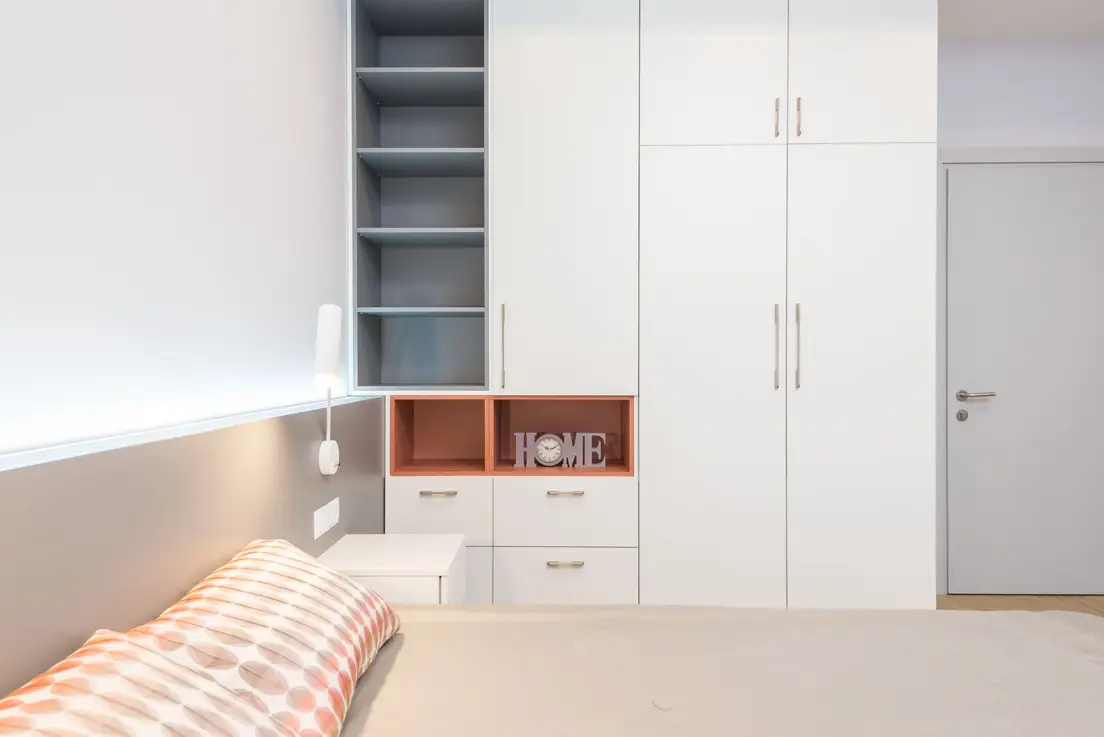 A white built-in wardrobe wall with open shelving and closed cabinets in a small bedroom