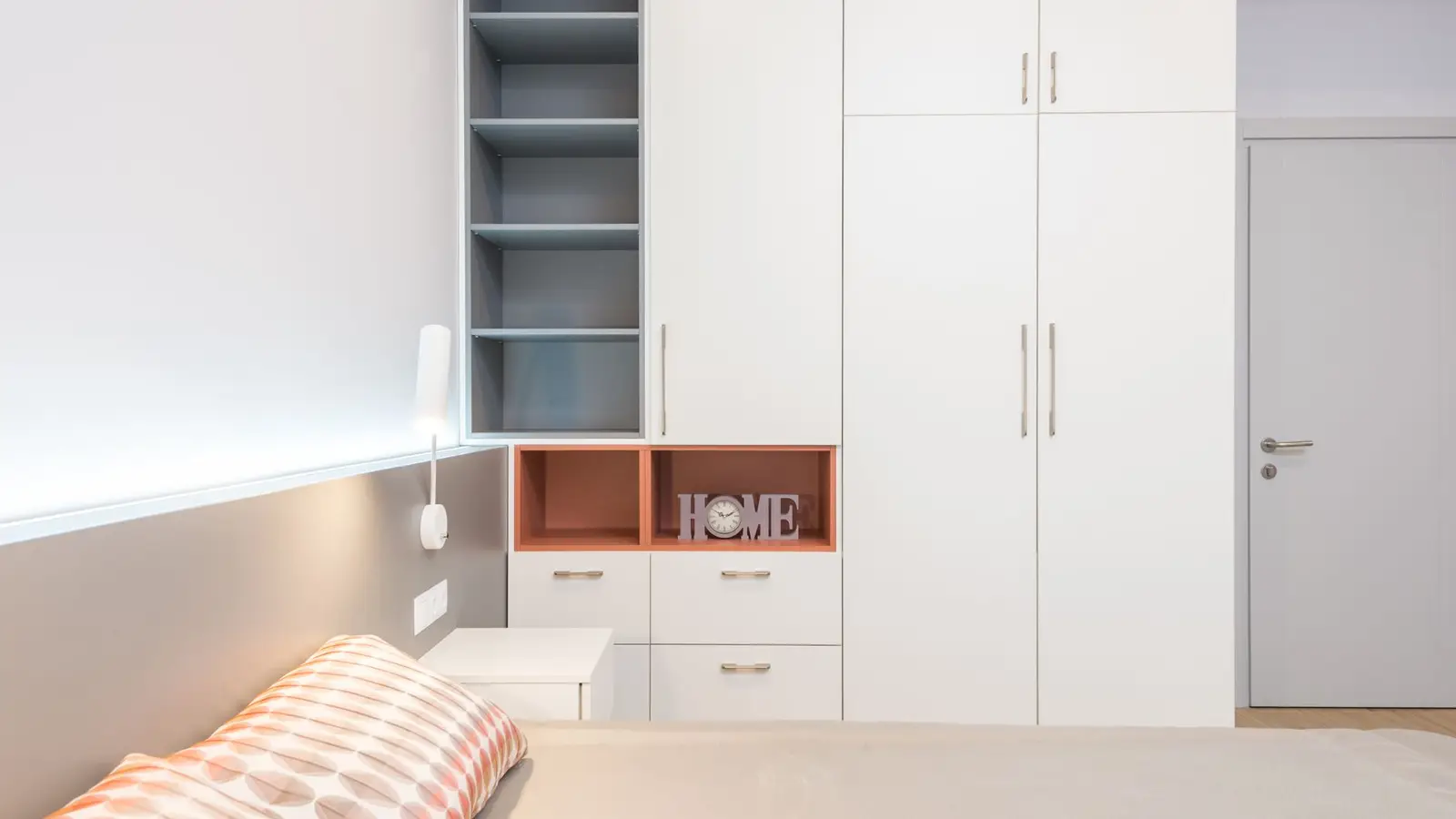 A white built-in wardrobe wall with open shelving and closed cabinets in a small bedroom