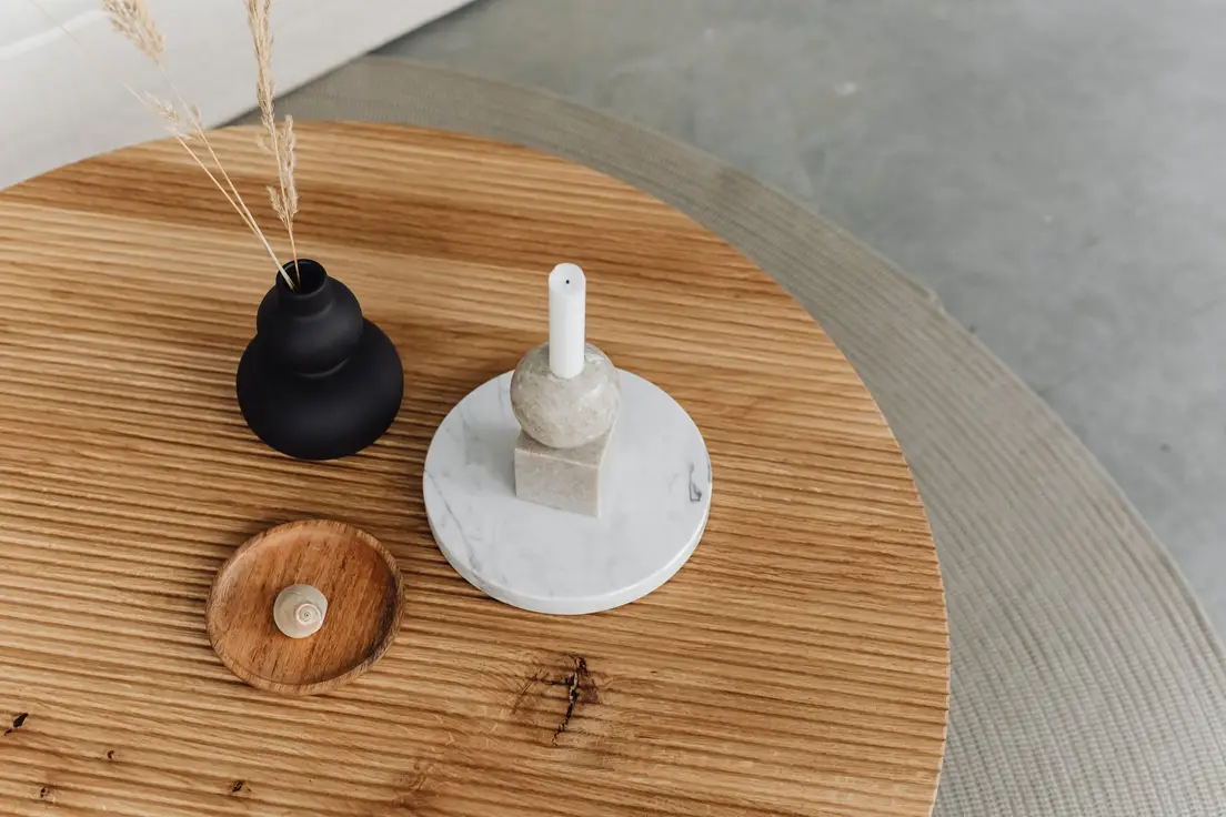 A round wood minimalist coffee table styled with a single candle and small vase