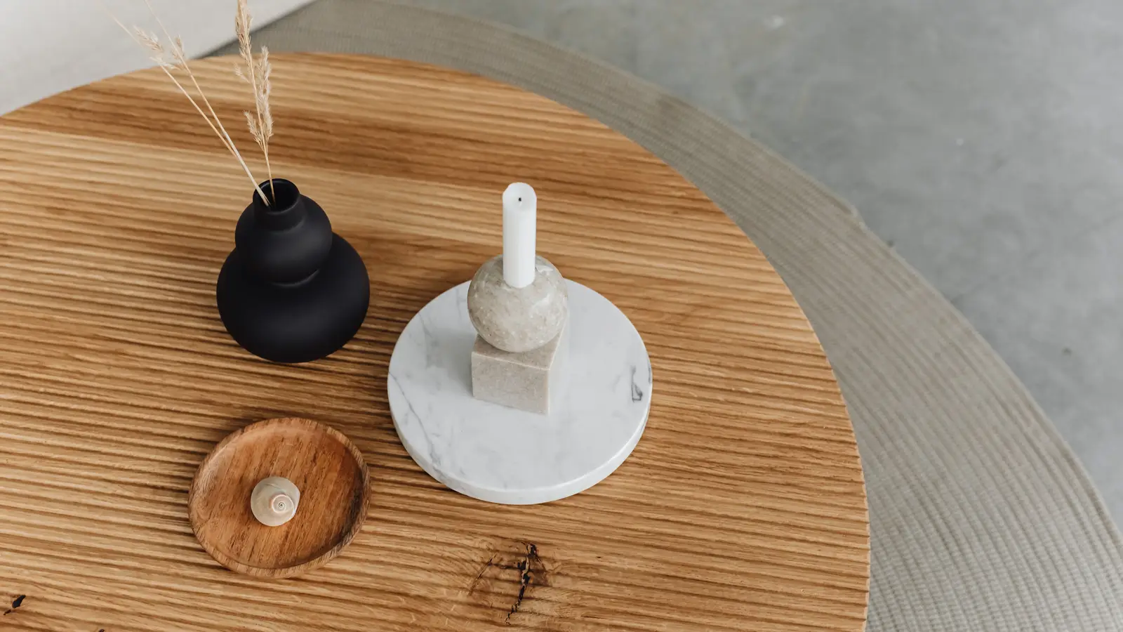 A round wood minimalist coffee table styled with a single candle and small vase
