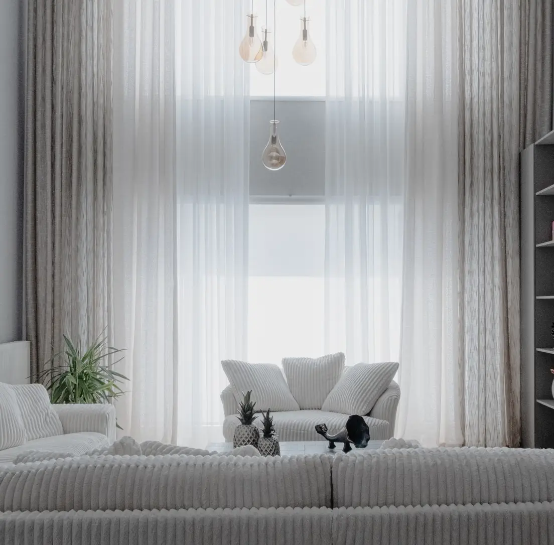 A bright, stark white living room with sheer curtains and pale cloud sofas, an example of cold minimalism