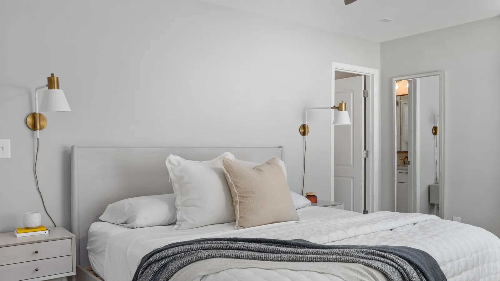 A neutral gray bedroom with cream and beige linen pillows against a plain wall