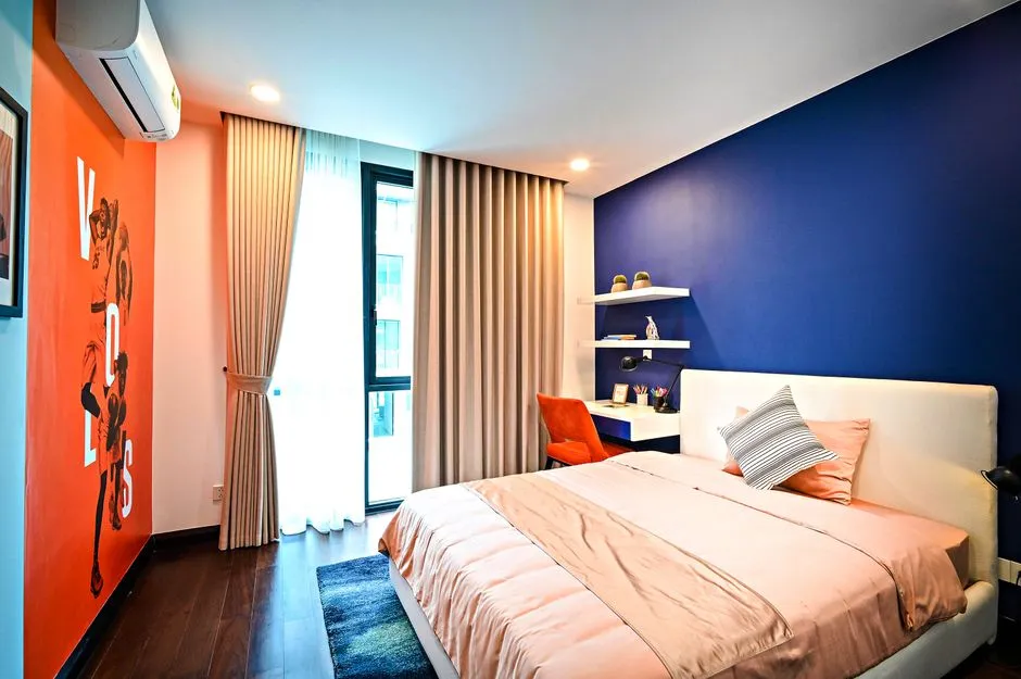 A colorful bedroom with a bold blue accent wall, an orange poster, and an orange desk chair
