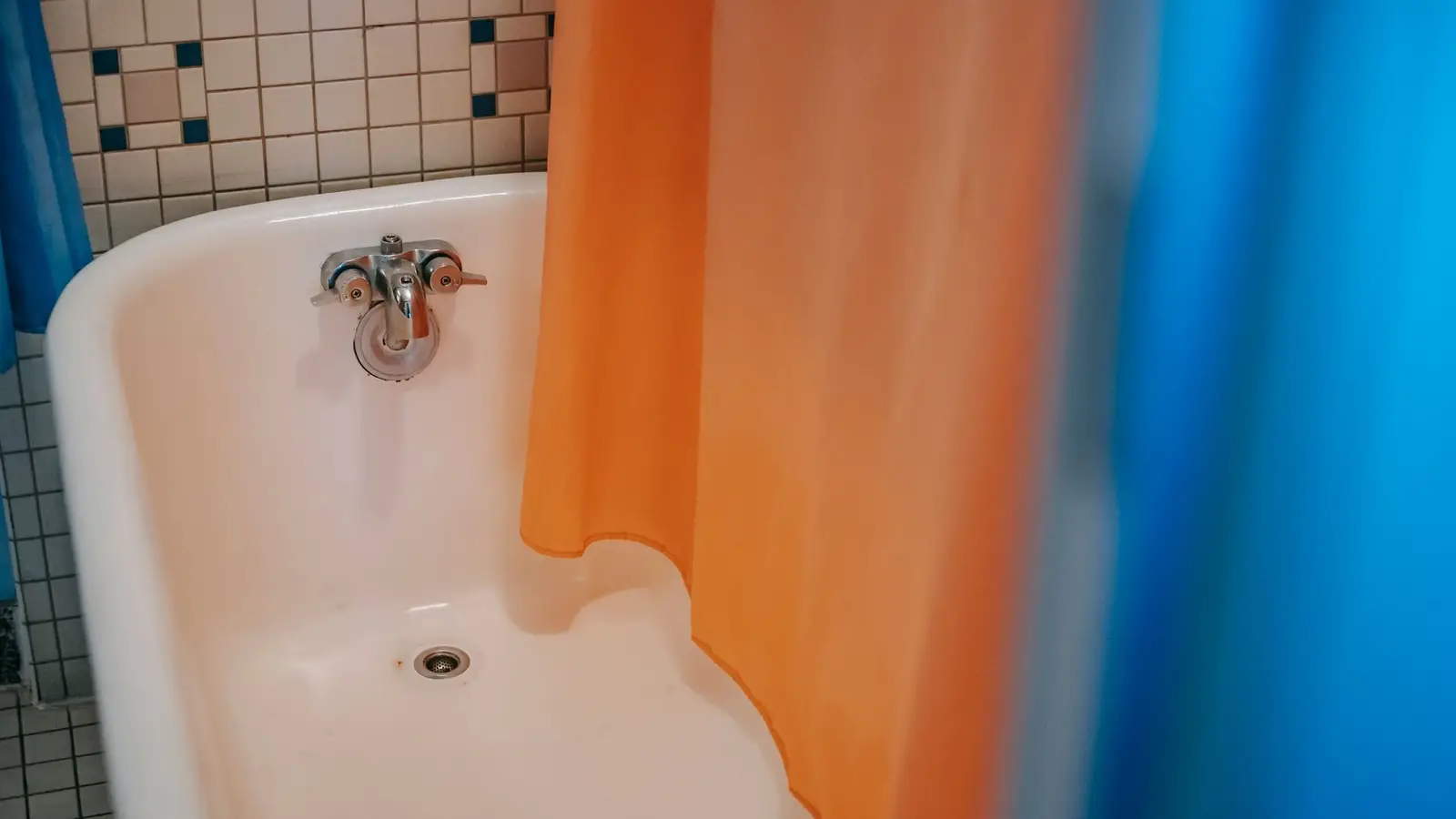 A small bathroom with a colorful orange and blue shower curtain over a vintage tub
