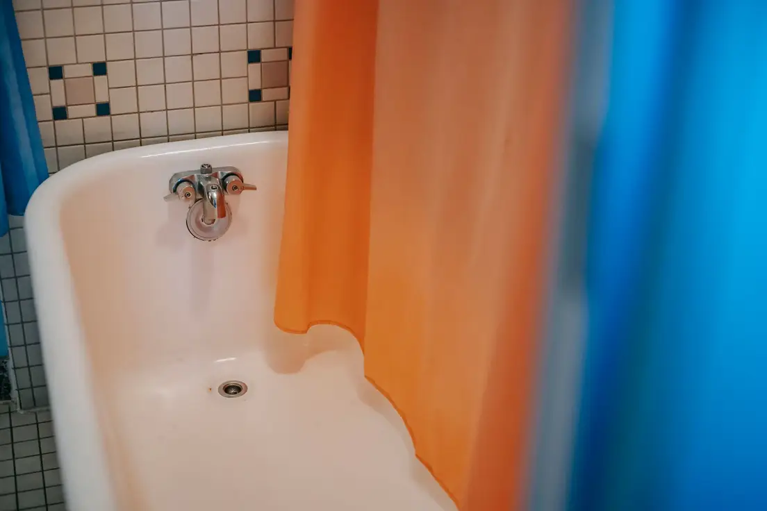 A small bathroom with a colorful orange and blue shower curtain over a vintage tub
