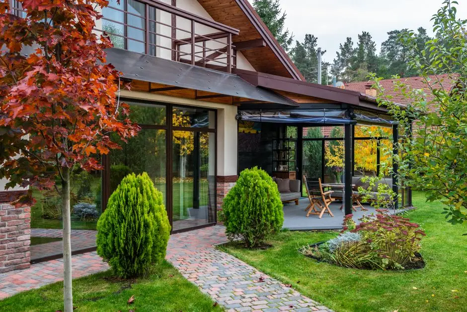 A house with an attached glass-covered patio below a balcony, connected by a paver walkway