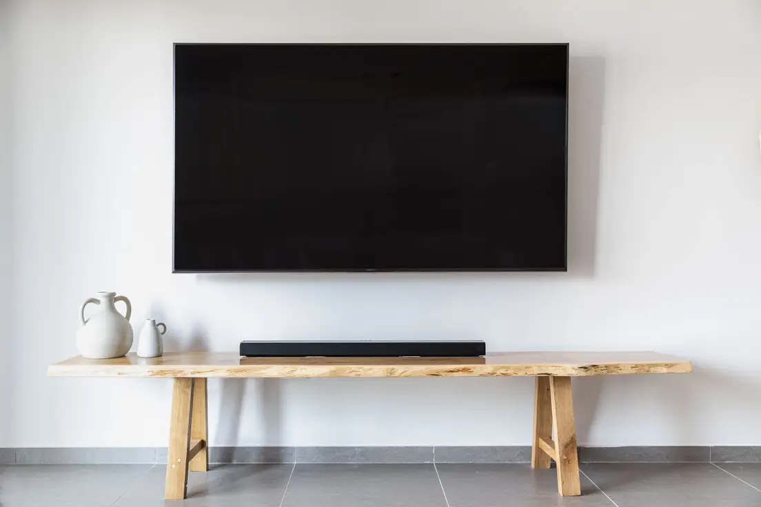 A wall-mounted TV above a minimal live-edge wood console with a soundbar and two ceramic vases