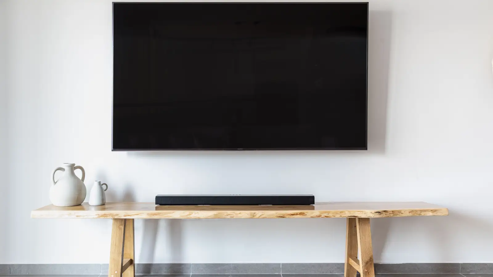 A wall-mounted TV above a minimal live-edge wood console with a soundbar and two ceramic vases