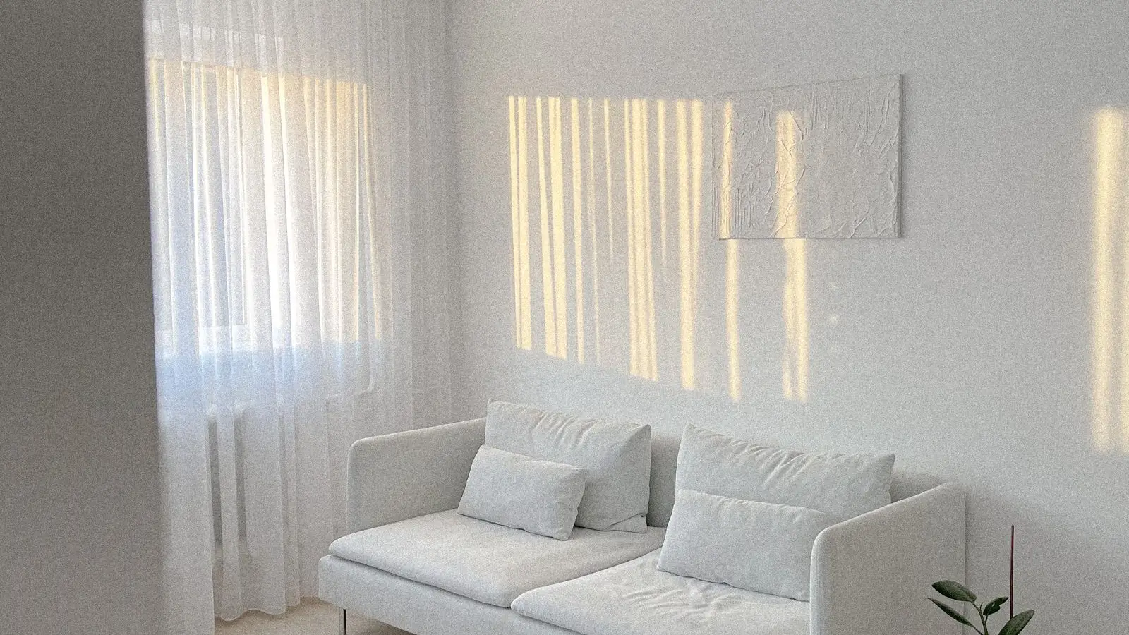 A stark, all-white minimalist living room with a pale sofa and bare walls, an example of cold minimalism without japandi's warmth