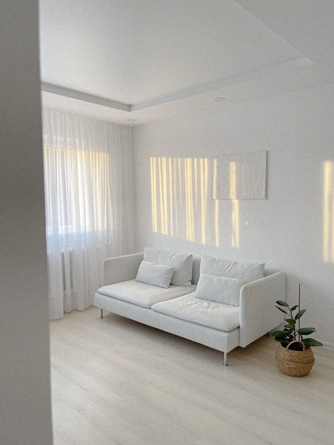 A stark, all-white minimalist living room with a pale sofa and bare walls, an example of cold minimalism without japandi's warmth