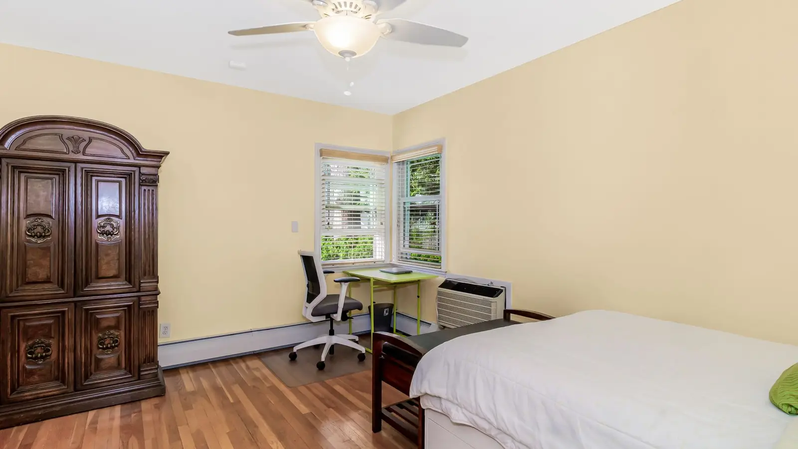 A small primary bedroom with the bed pushed into a corner to make room for a desk
