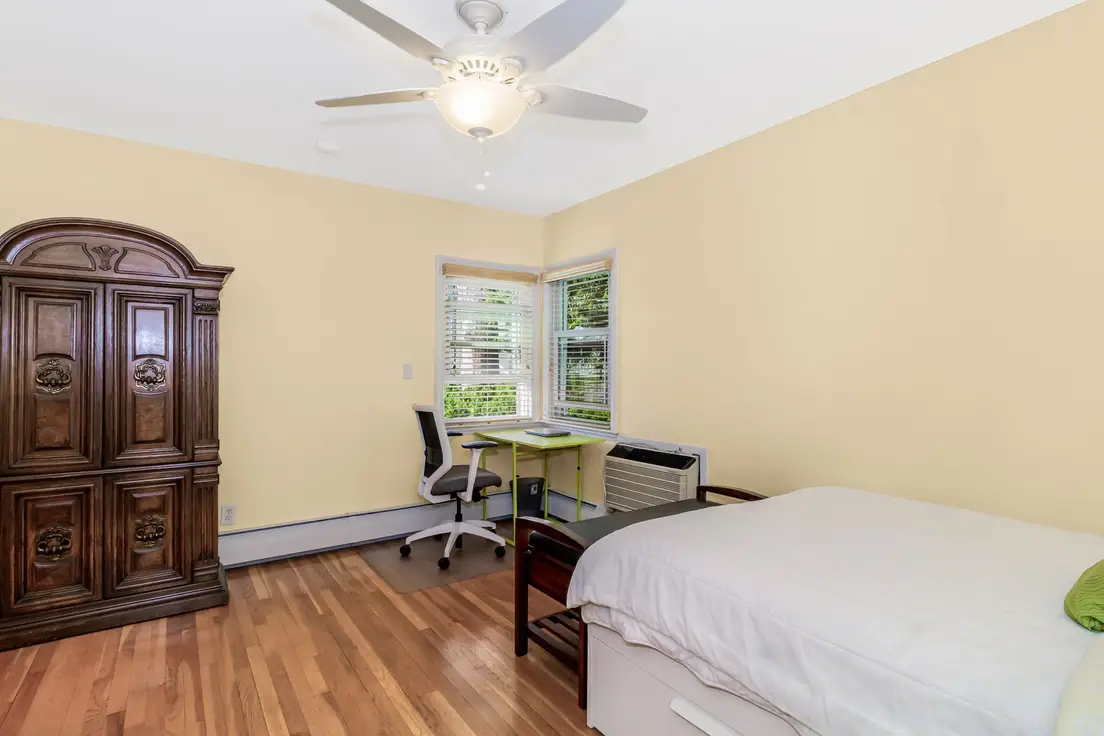 A small primary bedroom with the bed pushed into a corner to make room for a desk