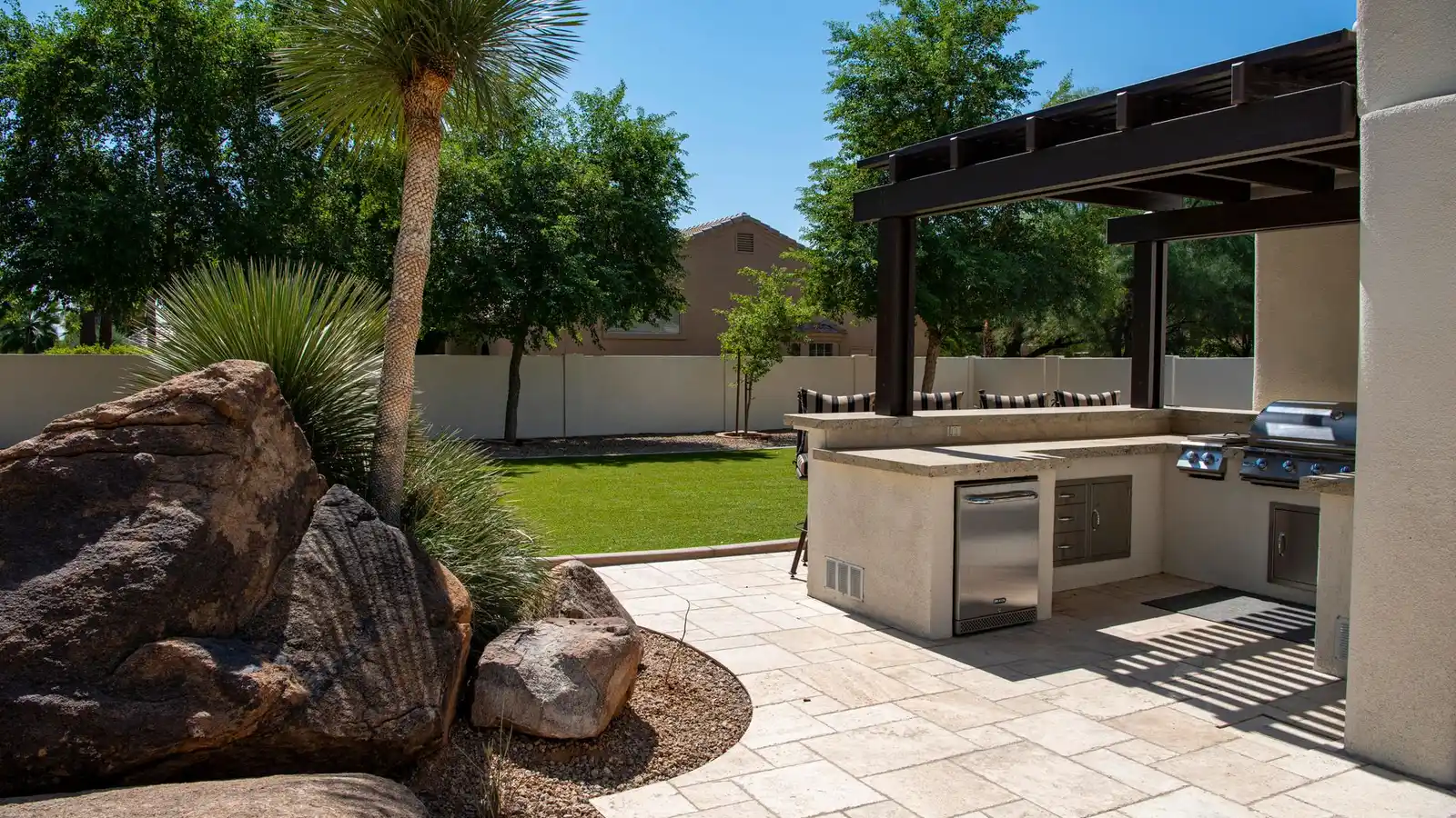 Outdoor kitchen prep counter with stainless steel grill and cabinets under a pergola