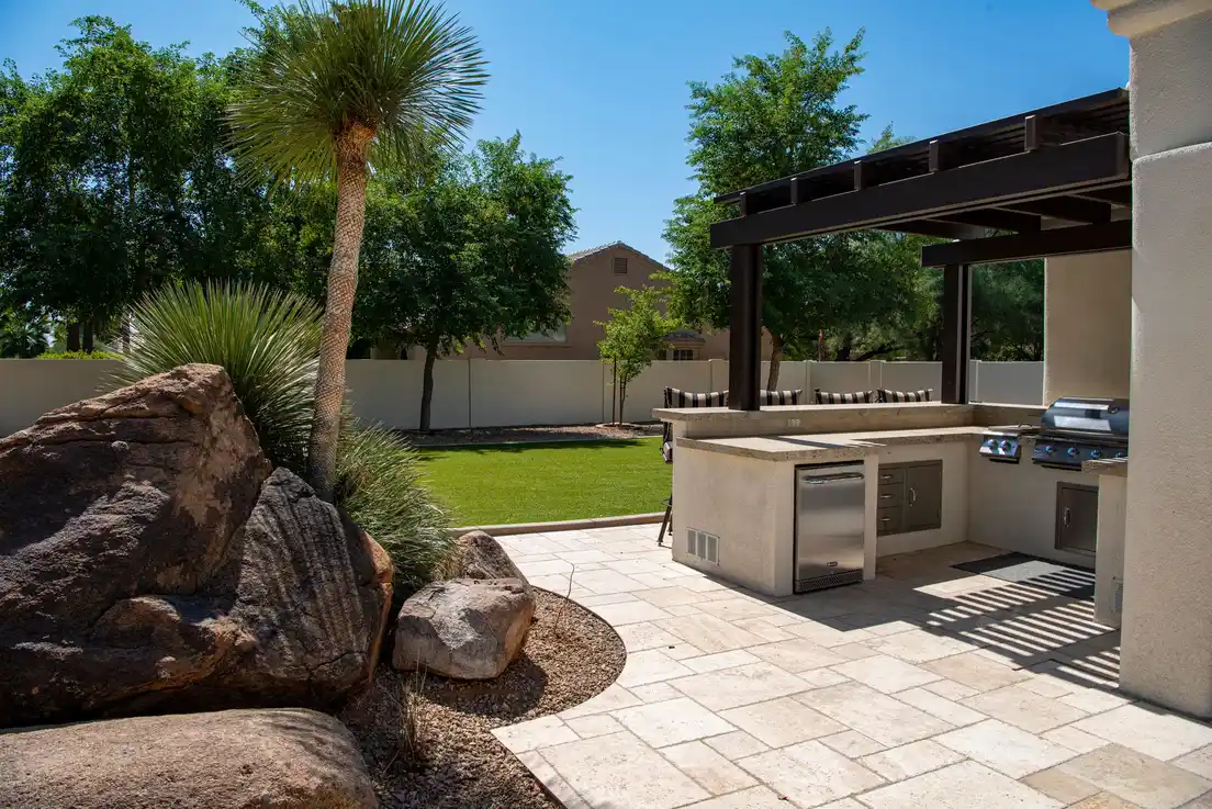 Outdoor kitchen prep counter with stainless steel grill and cabinets under a pergola