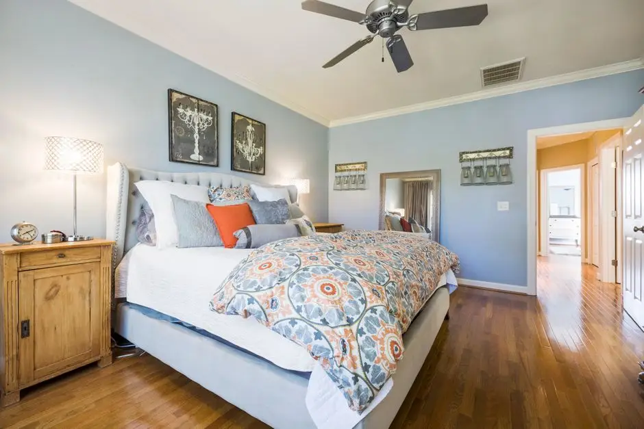 A primary bedroom with soft blue walls, crown molding, and a ceiling fan, an example of a good bedroom wall color for couples