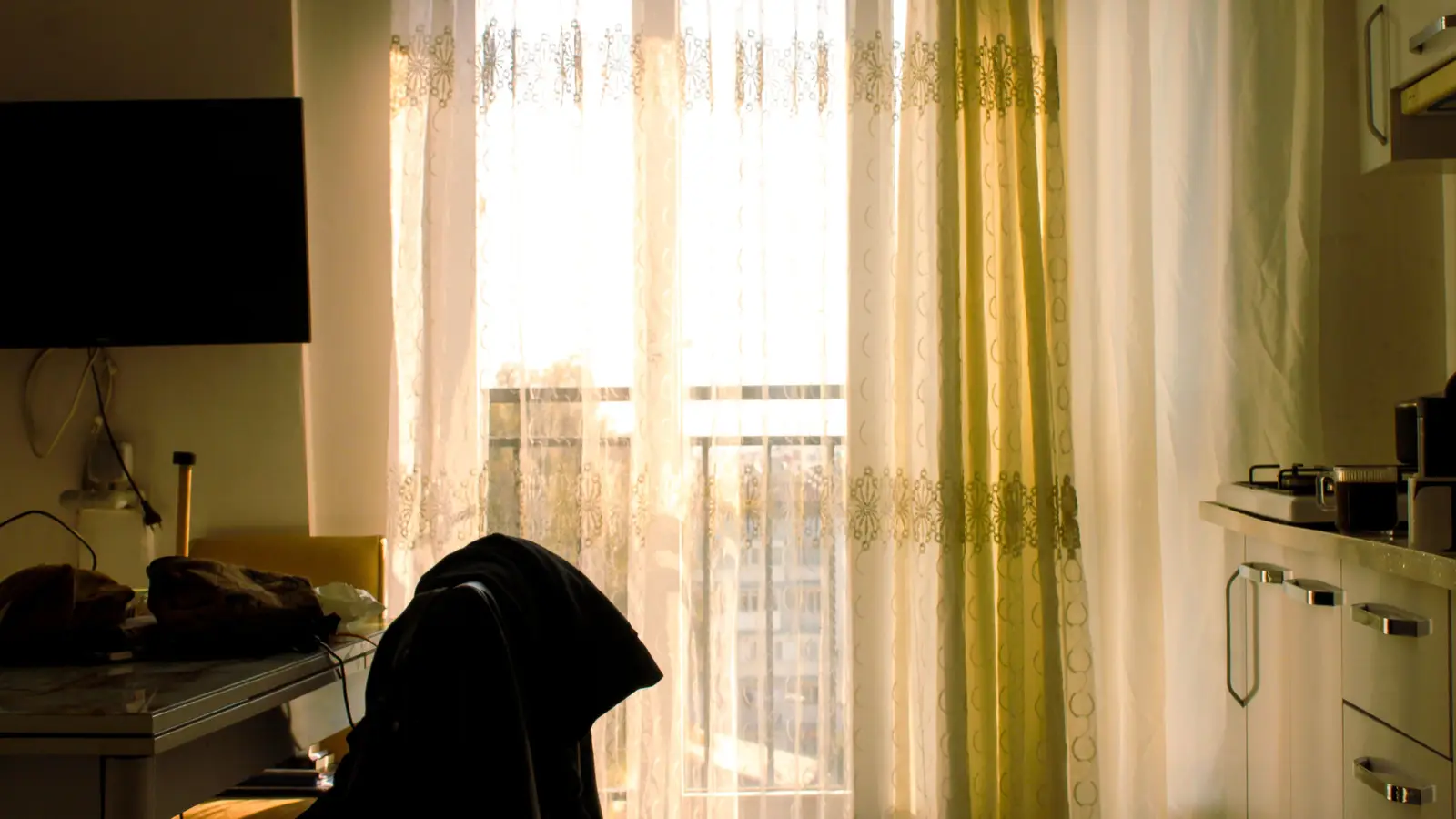A curtained window in a small apartment kitchen, letting daylight through while adding privacy