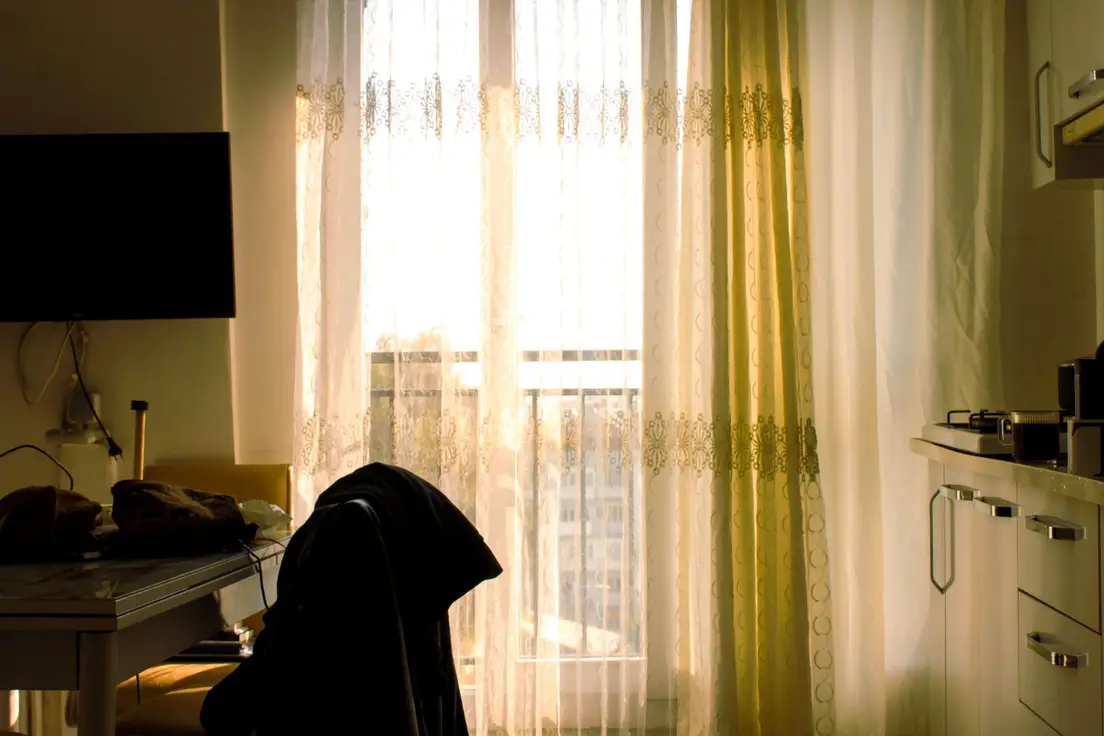 A curtained window in a small apartment kitchen, letting daylight through while adding privacy