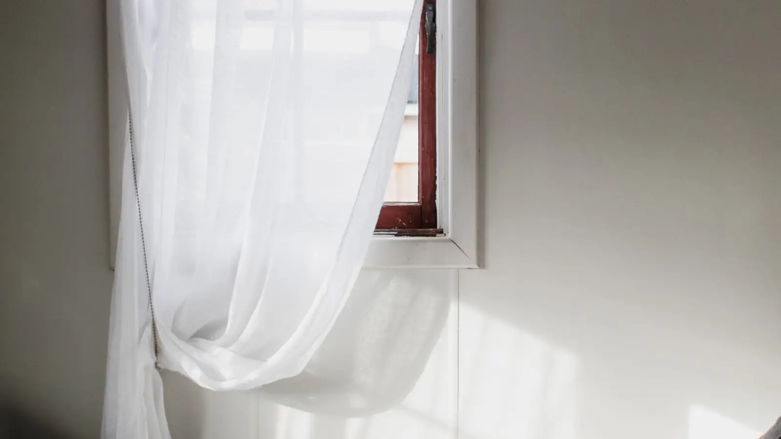 Sheer white linen curtains hanging in a sunlit bedroom window