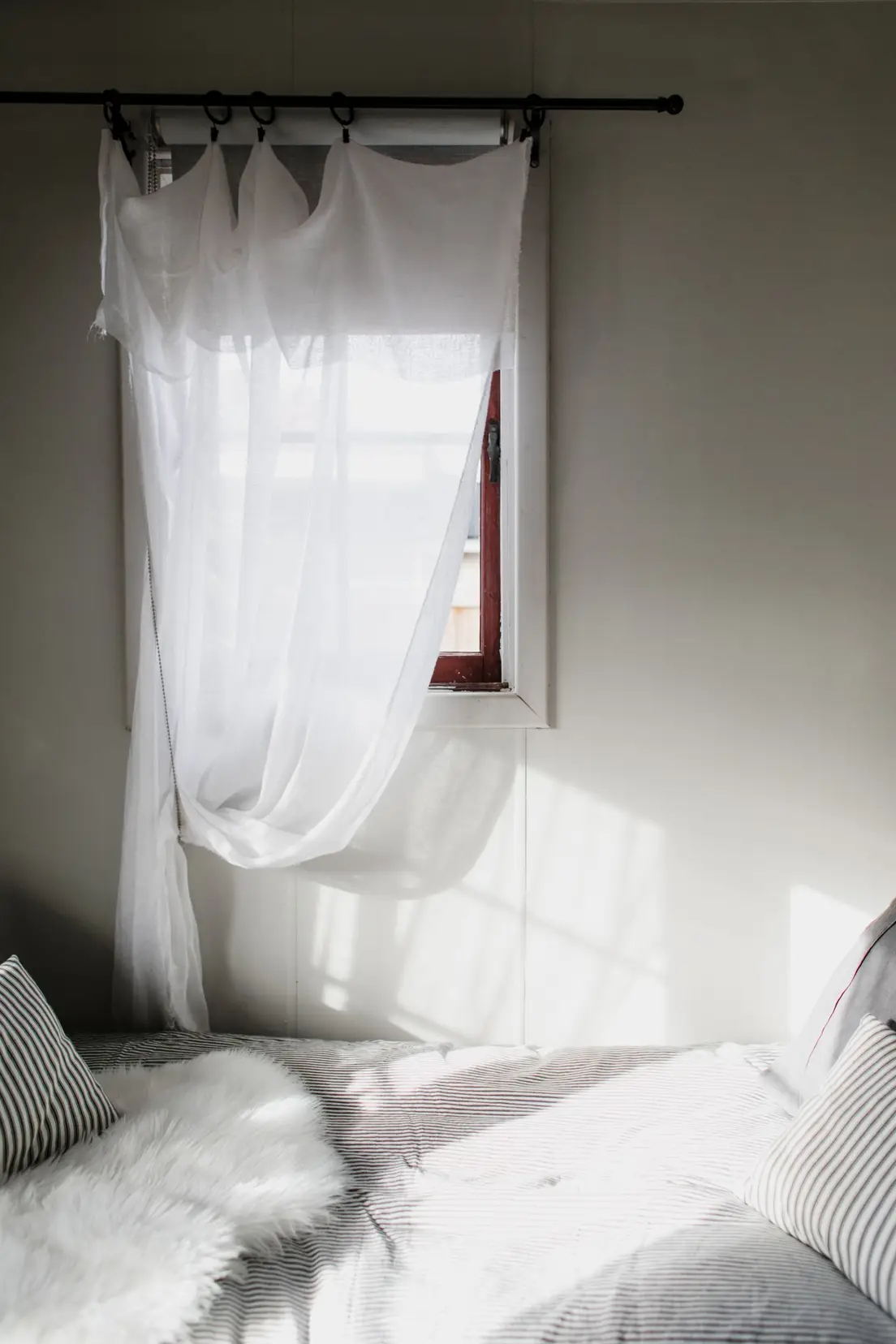 Sheer white linen curtains hanging in a sunlit bedroom window