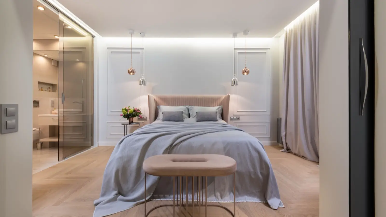 A curved blush pink wingback headboard with an oval pouf and copper pendant lights