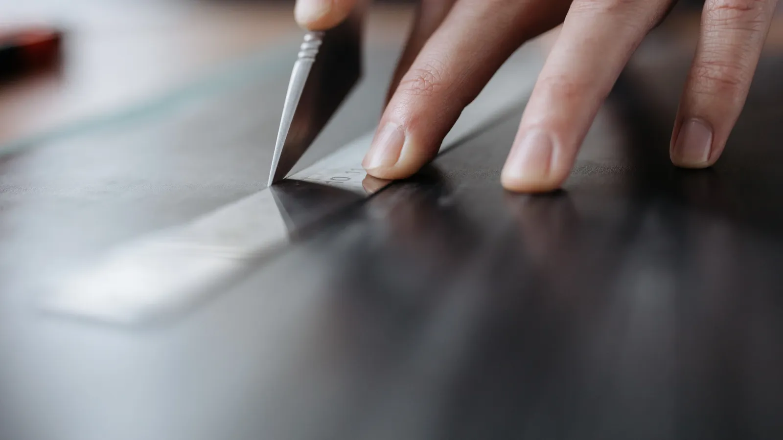 A hand using a utility knife and metal ruler to make a precise cut in a tile sheet