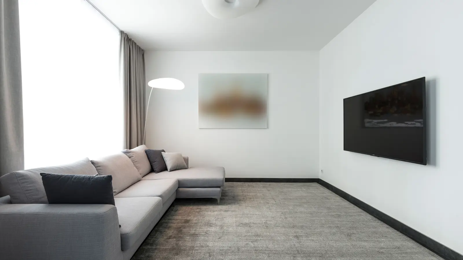 A spacious gray sectional sofa in an uncluttered minimalist living room with a wall-mounted TV