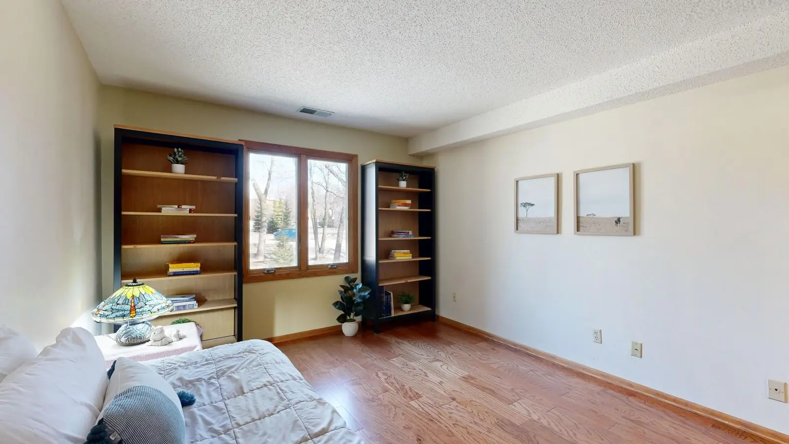 A tidy, uncluttered small bedroom with a built-in bookshelf and framed art