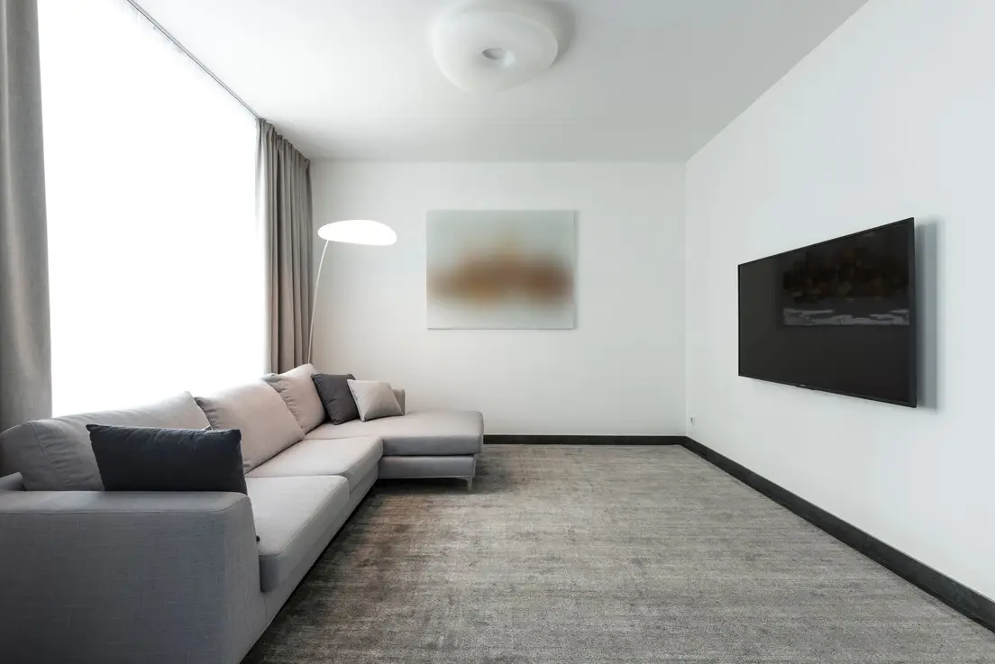 A spacious gray sectional sofa in an uncluttered minimalist living room with a wall-mounted TV