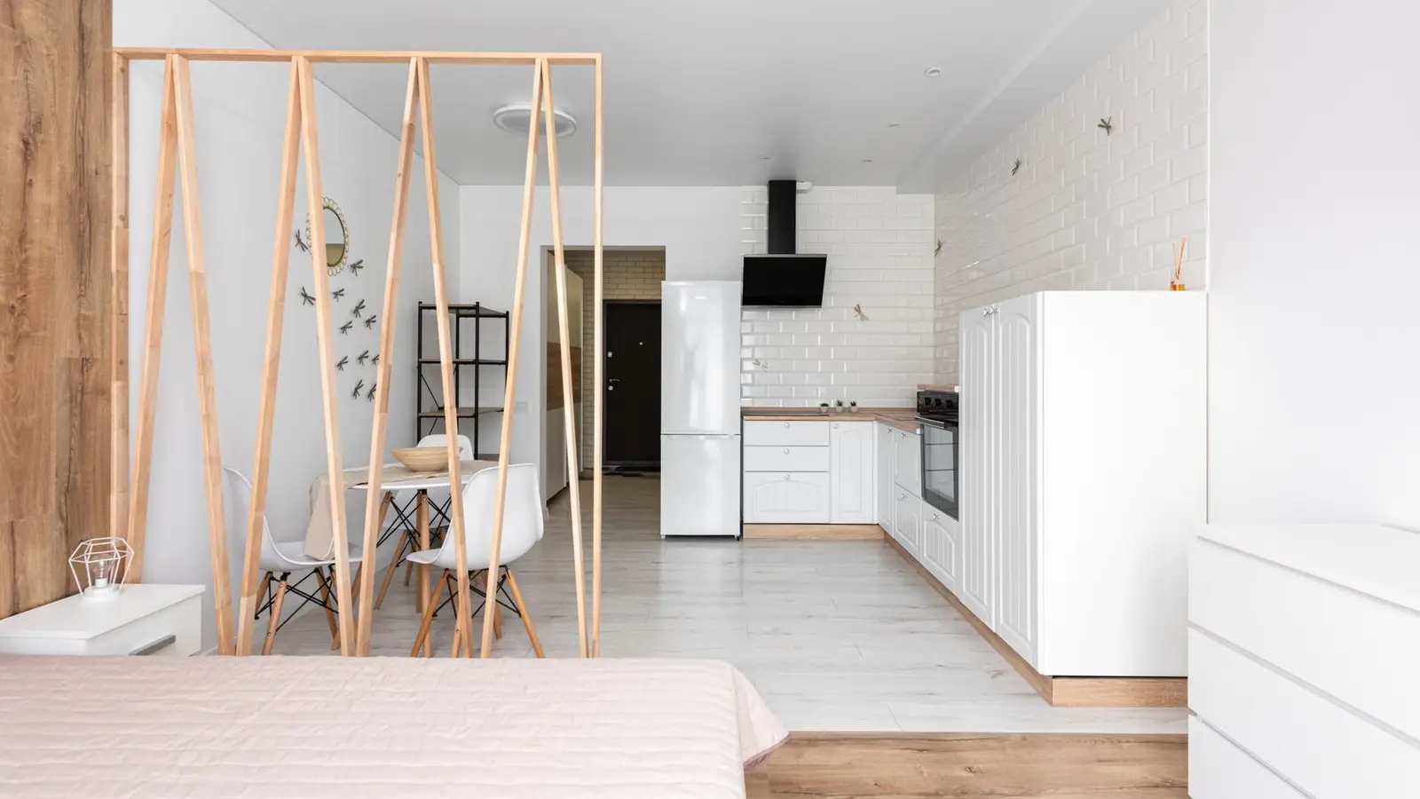 A freestanding wooden slat room divider separating a small apartment's living space from its kitchen