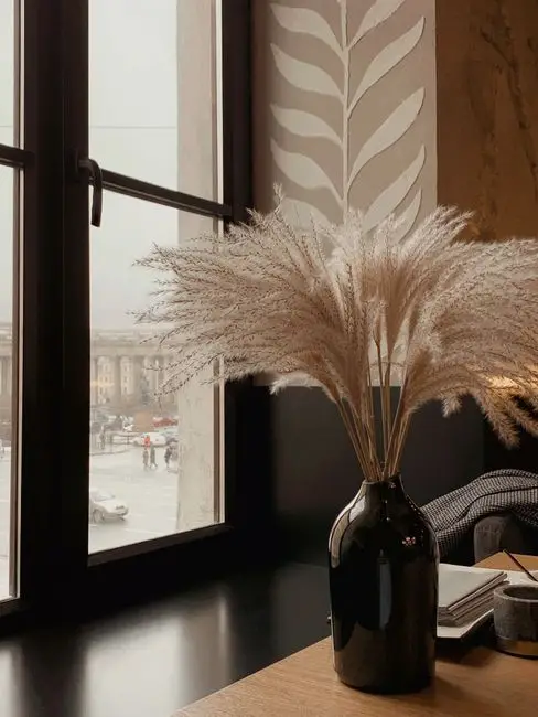 Dried pampas grass in a dark ceramic vase near a window, an organic modern living room decor idea