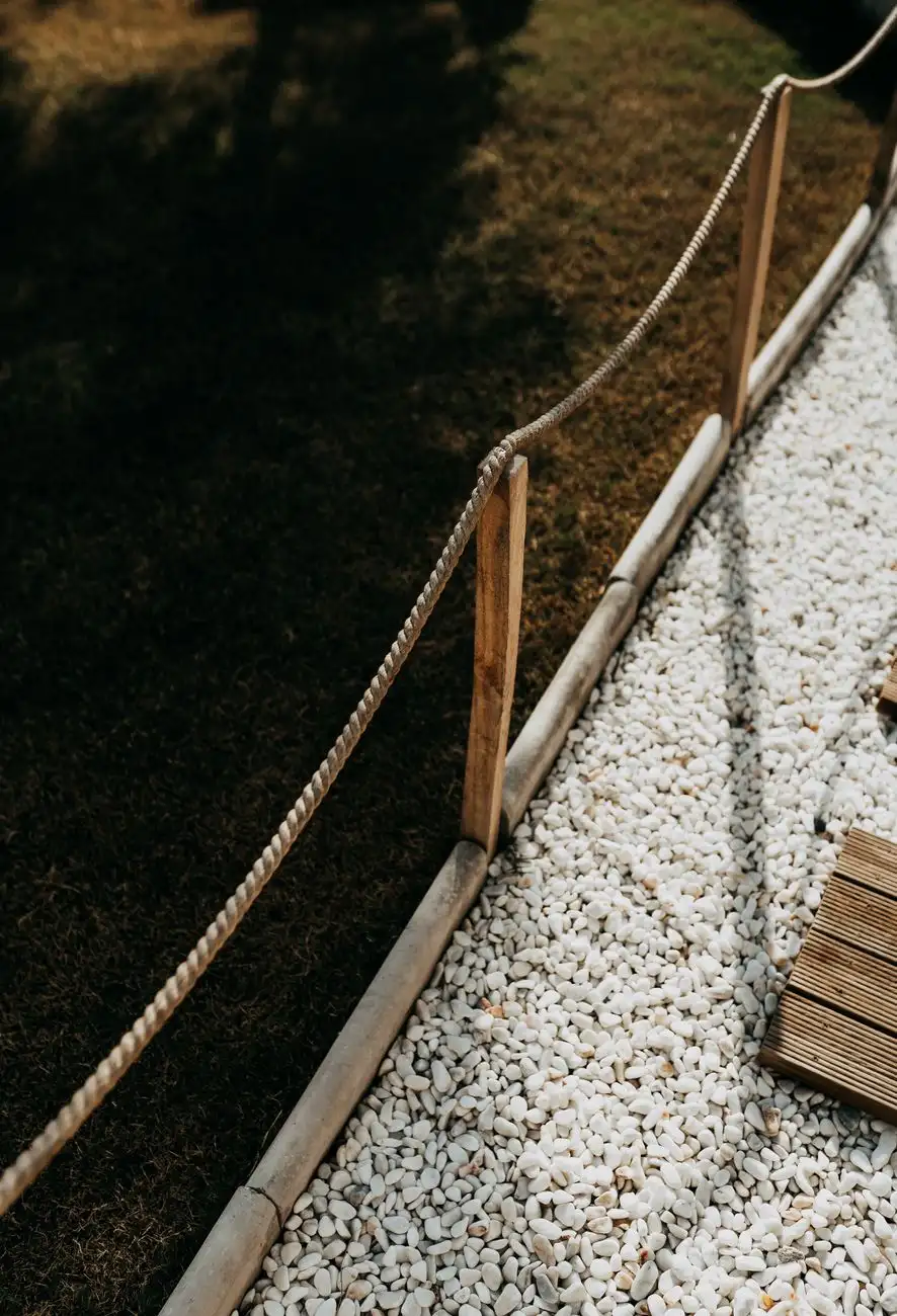 A rope-and-stake garden edging separating a lawn from a pea gravel path
