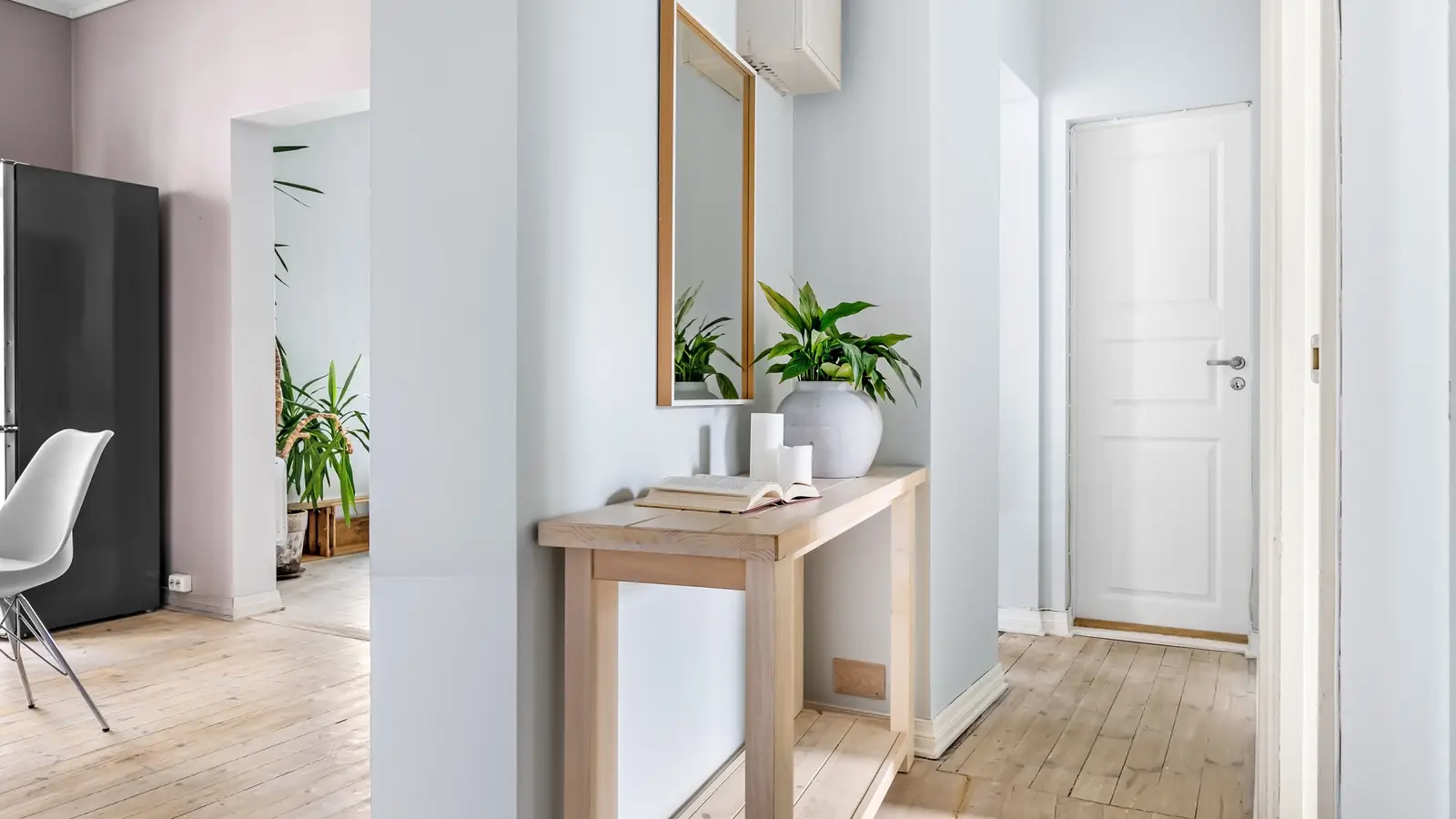 A narrow wood console table with a mirror above it in a small apartment entryway