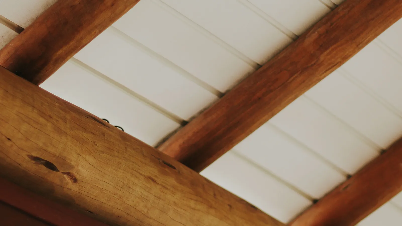 A rustic exposed wood beam against a white shiplap ceiling in a farmhouse kitchen