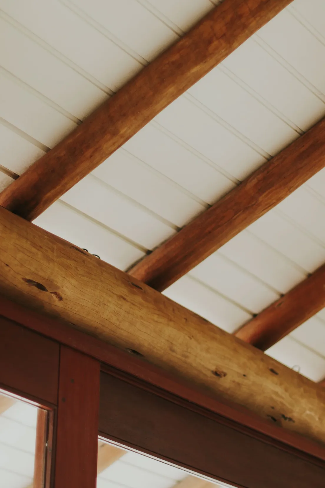 A rustic exposed wood beam against a white shiplap ceiling in a farmhouse kitchen
