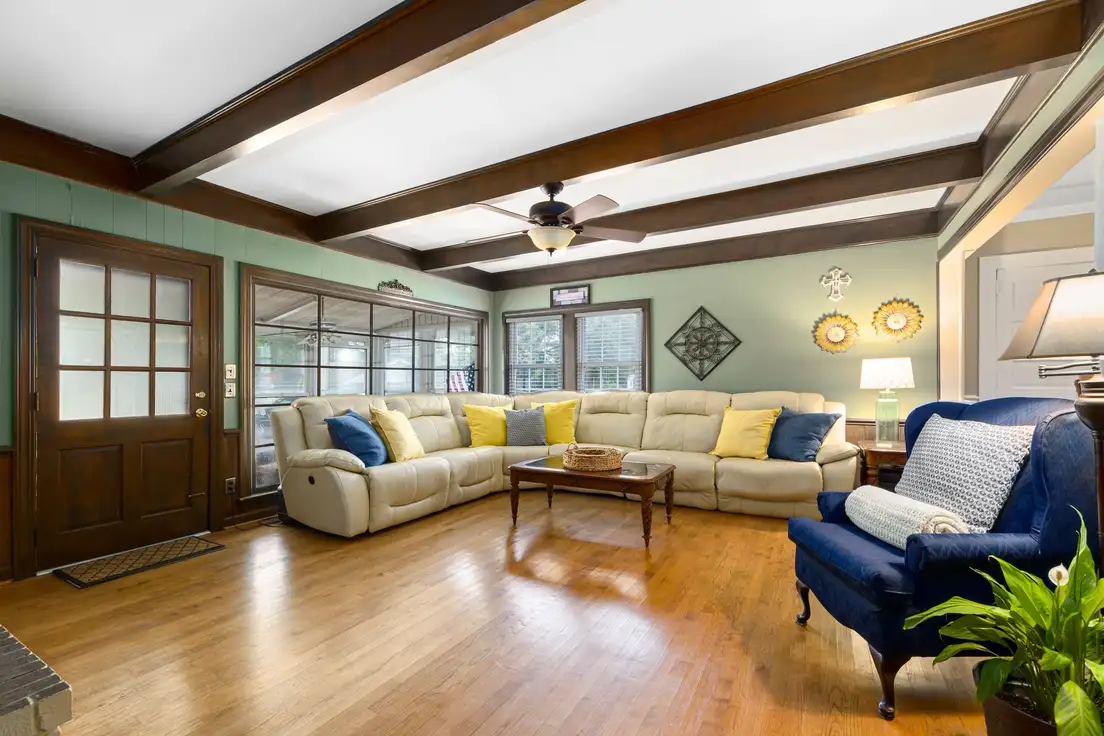 Dark stained wood beams running across the ceiling of a living room with a cream sectional, showing how heavy beams look on a standard ceiling