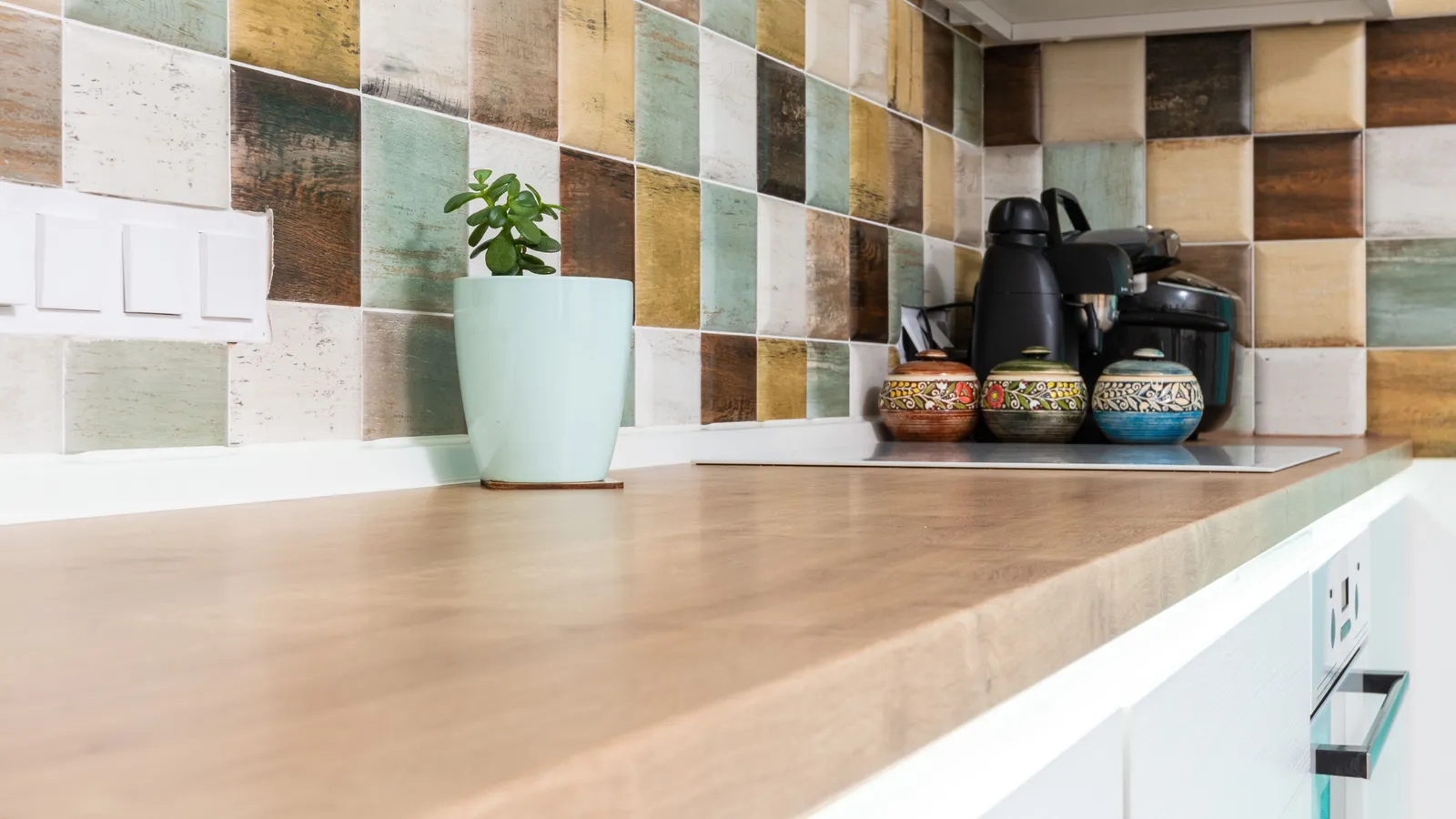 A finished patterned tile backsplash meeting a wood counter at a corner near an outlet