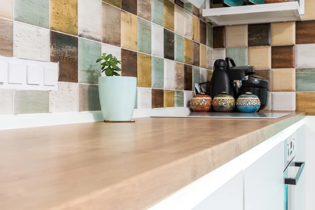 A finished patterned tile backsplash meeting a wood counter at a corner near an outlet