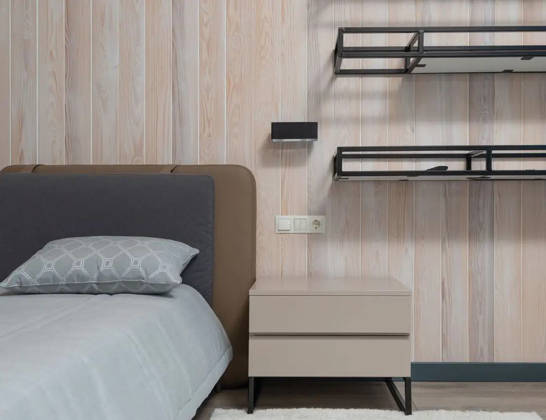 A floating wall shelf and a slim nightstand beside a bed in a small bedroom
