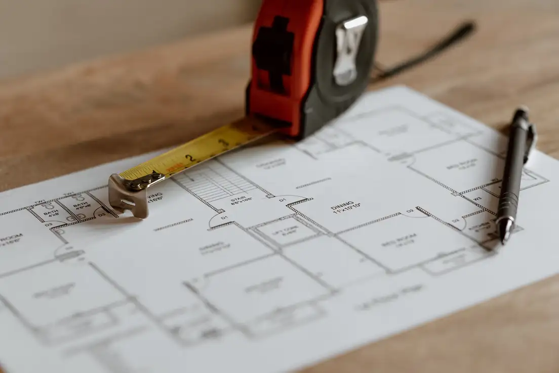 A tape measure and pen on a printed floor plan showing a dining room, used to plan a small living room dining room combo layout