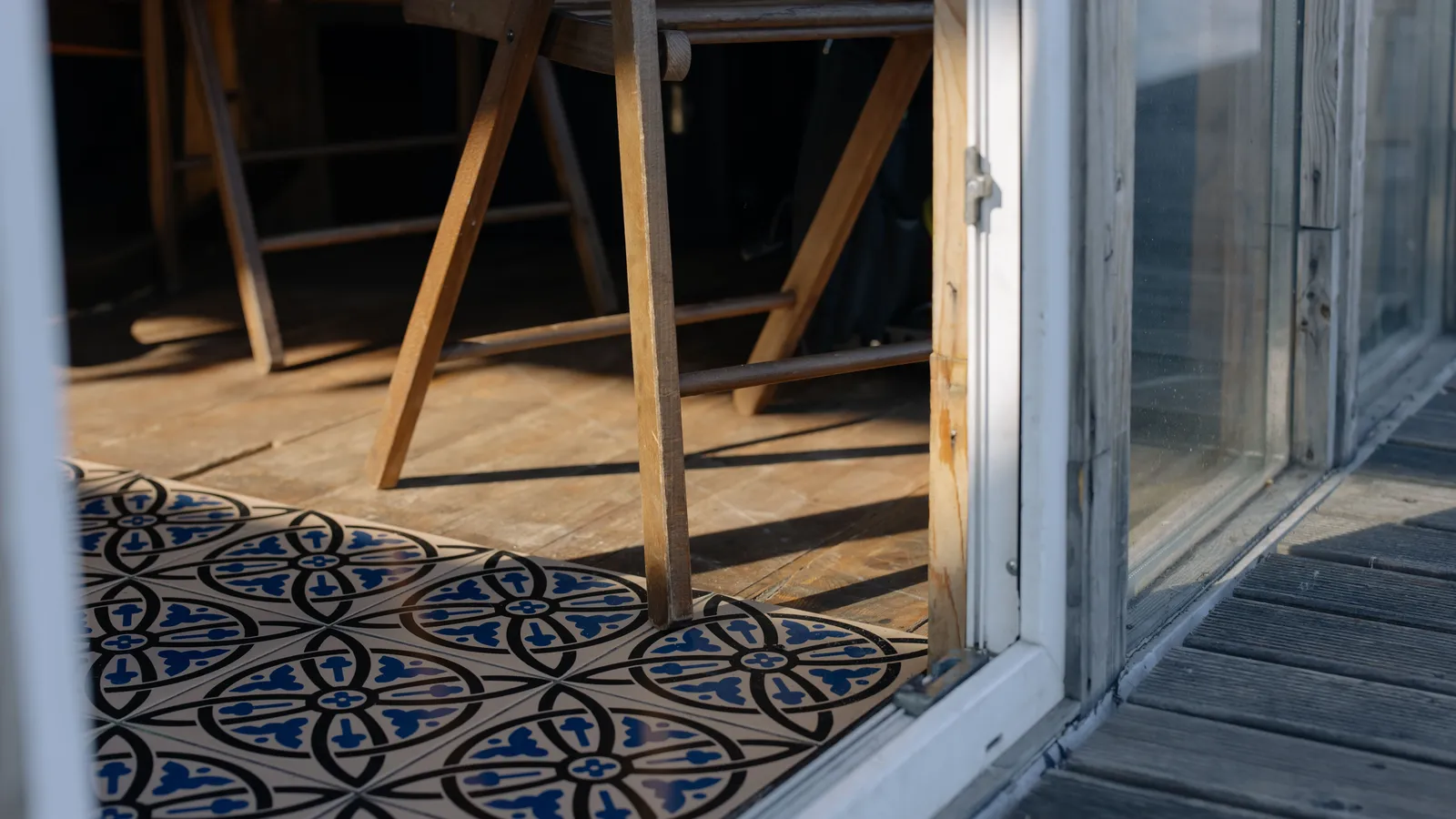 A wooden folding chair on a small balcony with interlocking wood deck tiles and a patterned rug