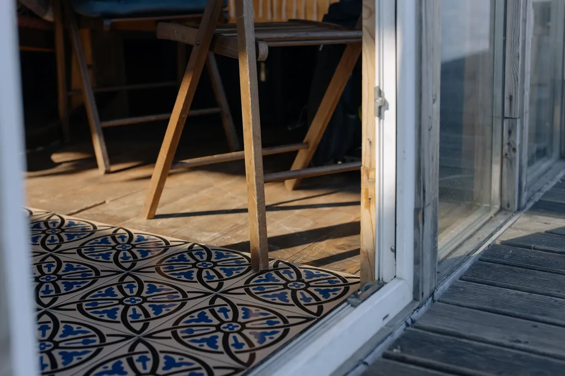 A wooden folding chair on a small balcony with interlocking wood deck tiles and a patterned rug