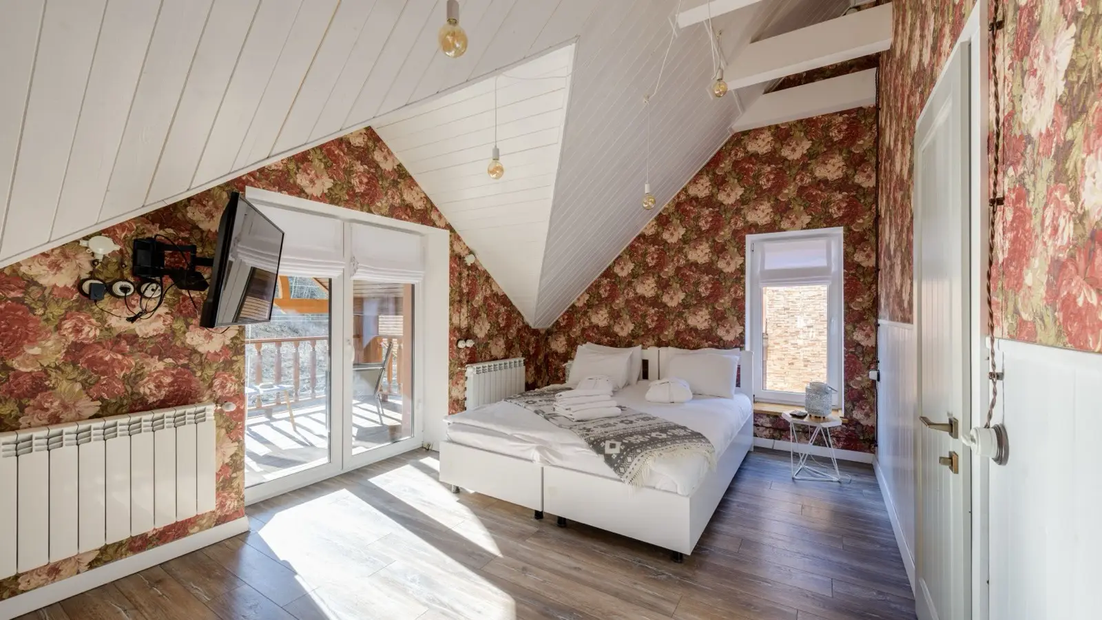 A bedroom with red and cream floral wallpaper covering the walls and sloped ceiling