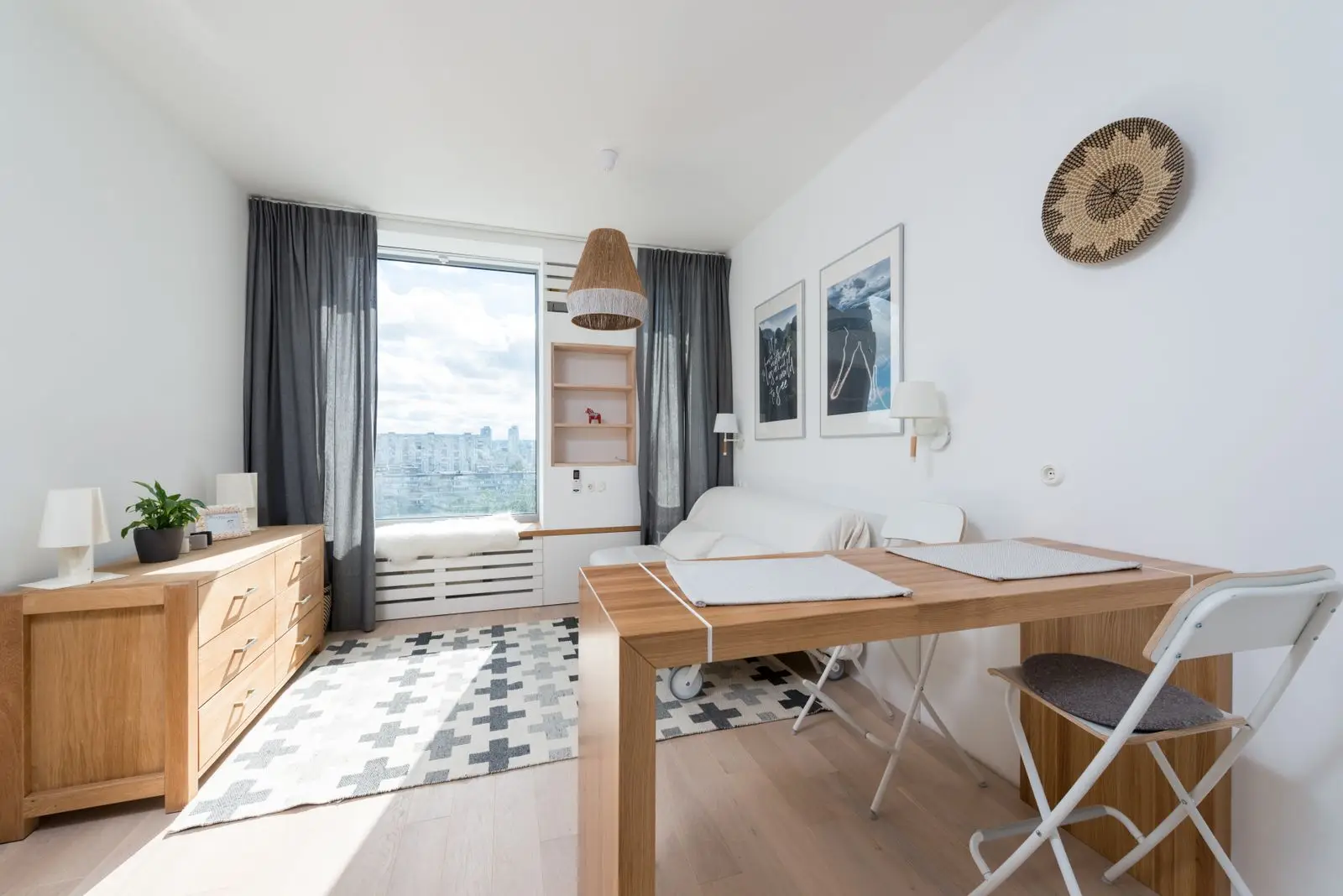 A compact fold-away desk with folding chairs against a window in a small apartment, a multifunctional home office setup