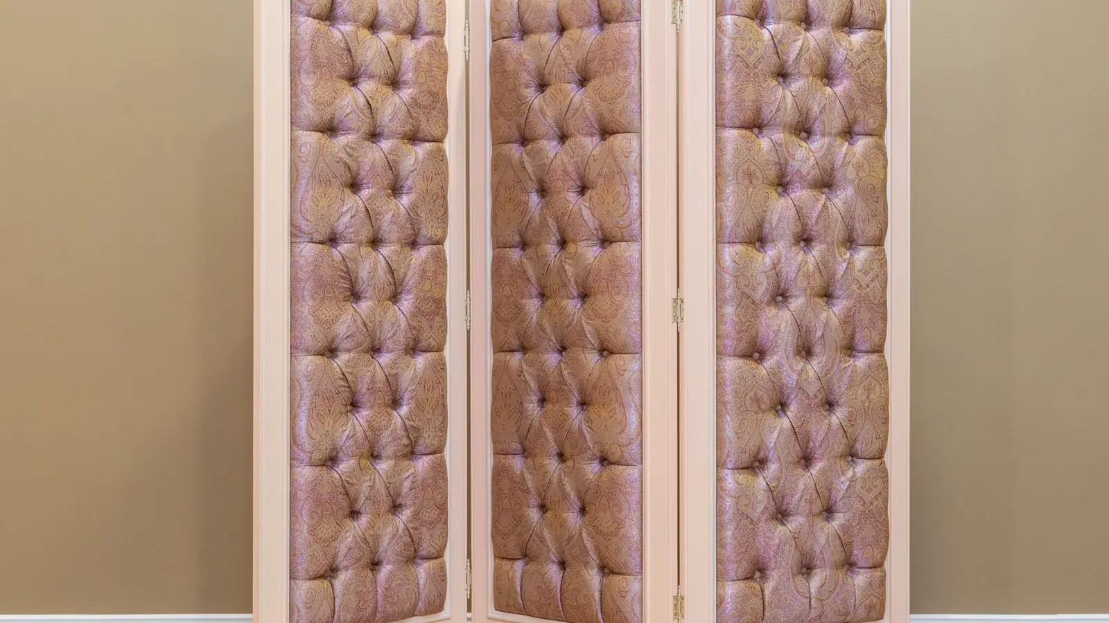 A three-panel upholstered folding screen used as a room divider in a bedroom corner