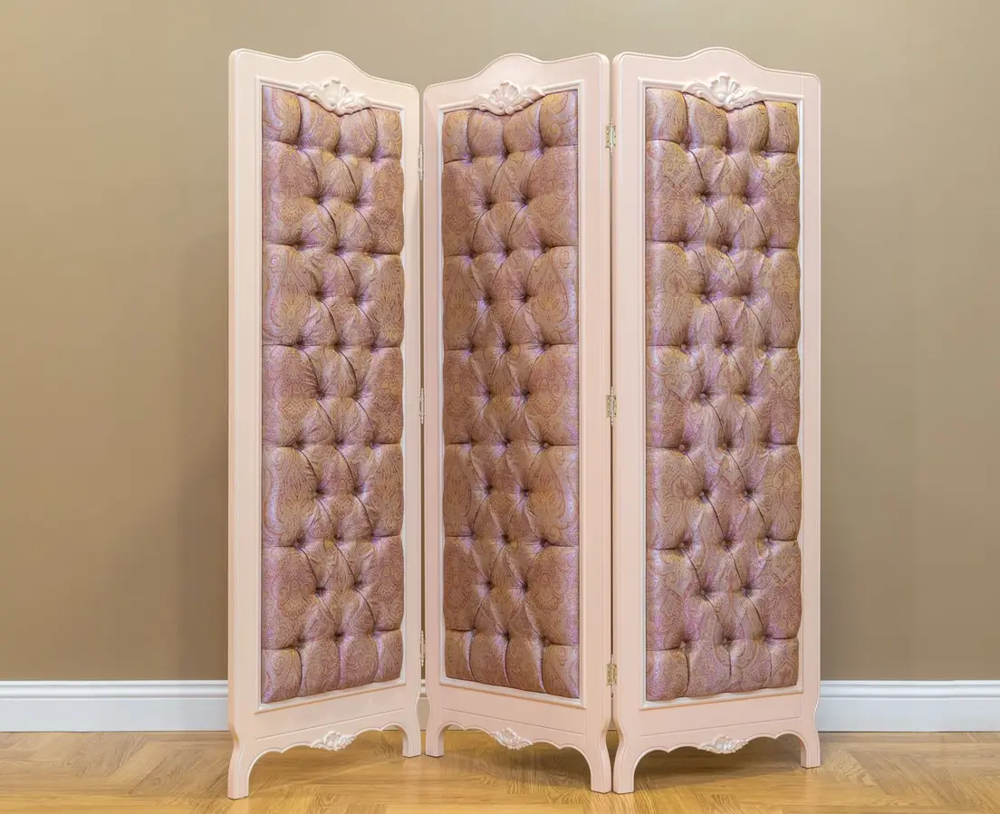 A three-panel upholstered folding screen used as a room divider in a bedroom corner