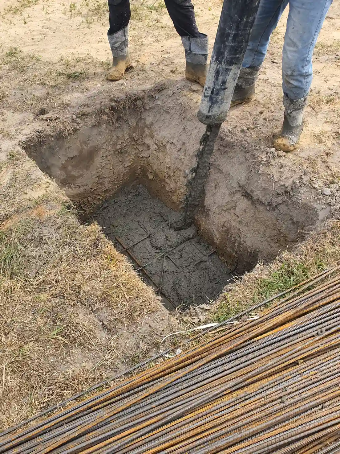 A concrete footing being poured into a post hole with rebar for a patio cover structure
