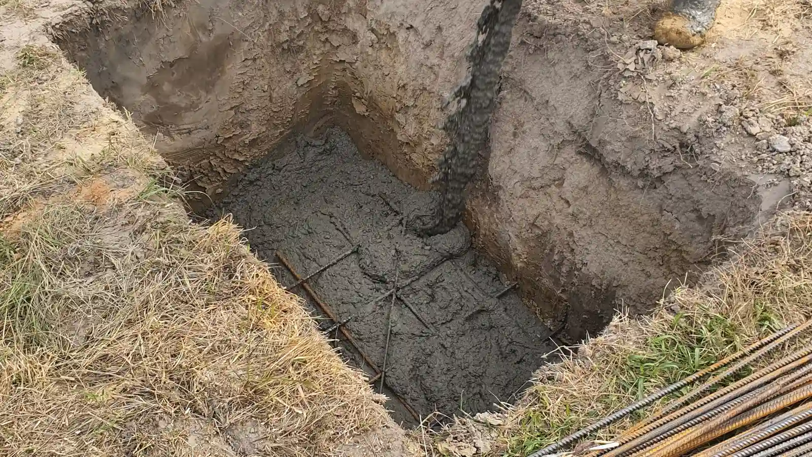 A concrete footing being poured into a post hole with rebar for a patio cover structure