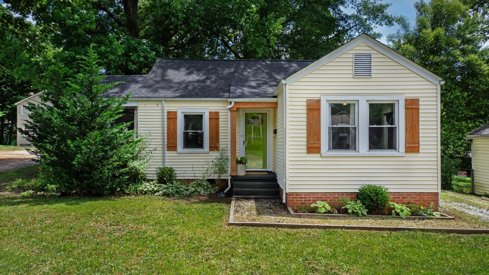 A yellow house exterior with a single repeated shrub shape along the foundation planting bed