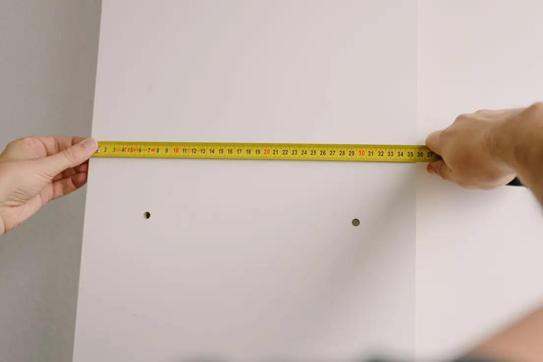 A person measuring a wood stud board with a tape measure while framing a temporary wall