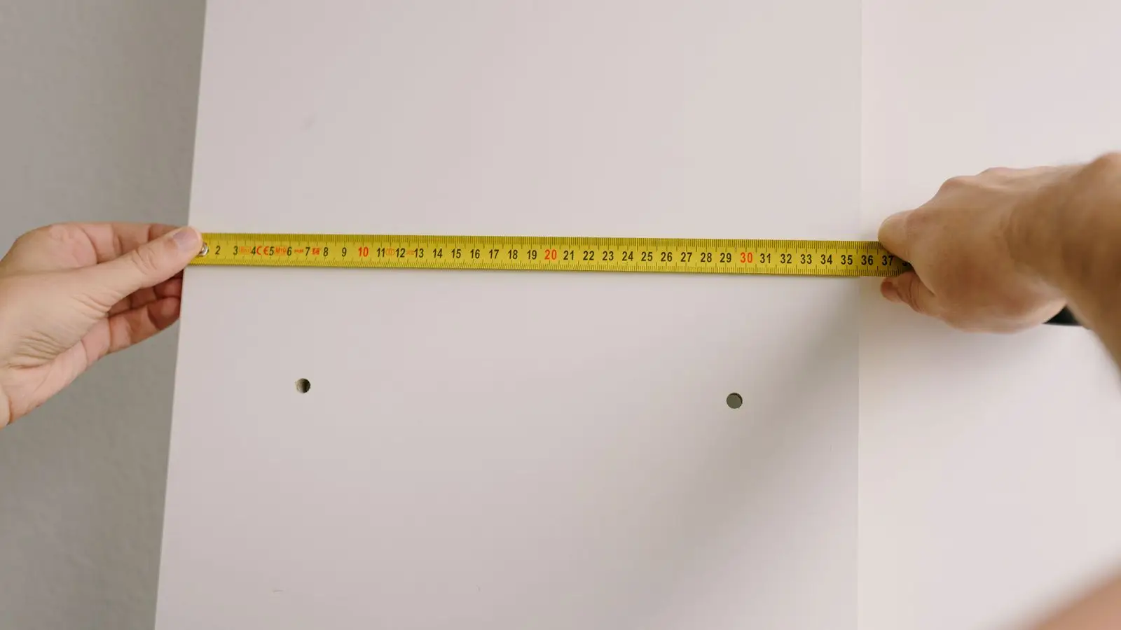A person measuring a wood stud board with a tape measure while framing a temporary wall